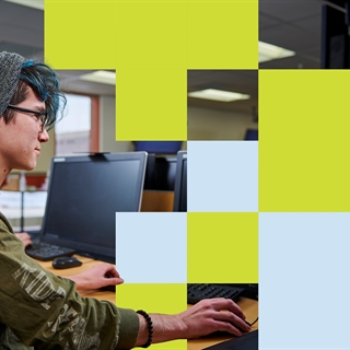 student with glasses and a beanie works at a computer