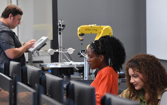 Students working with computers and robotic arm