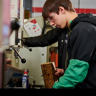 male student in a black hoodie working with manufacturing equipment